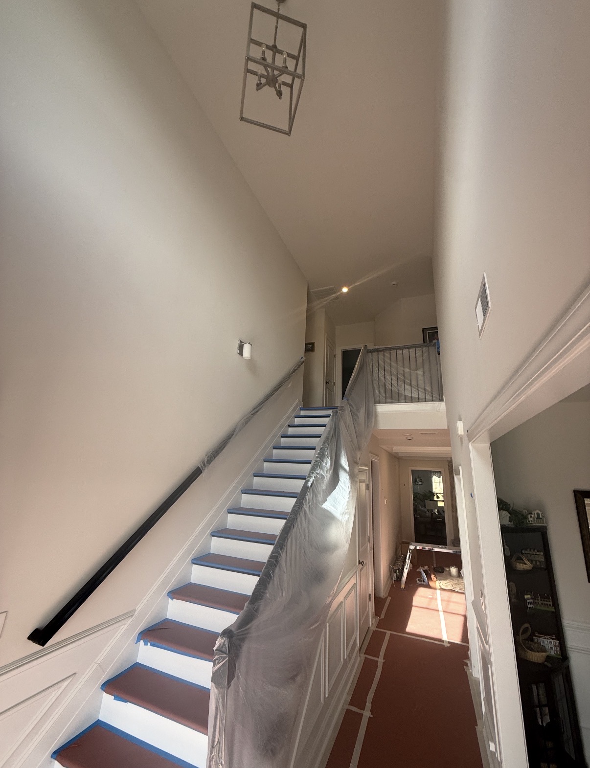 Two-story stairwell with white walls and trim masked and painted during an interior painting project